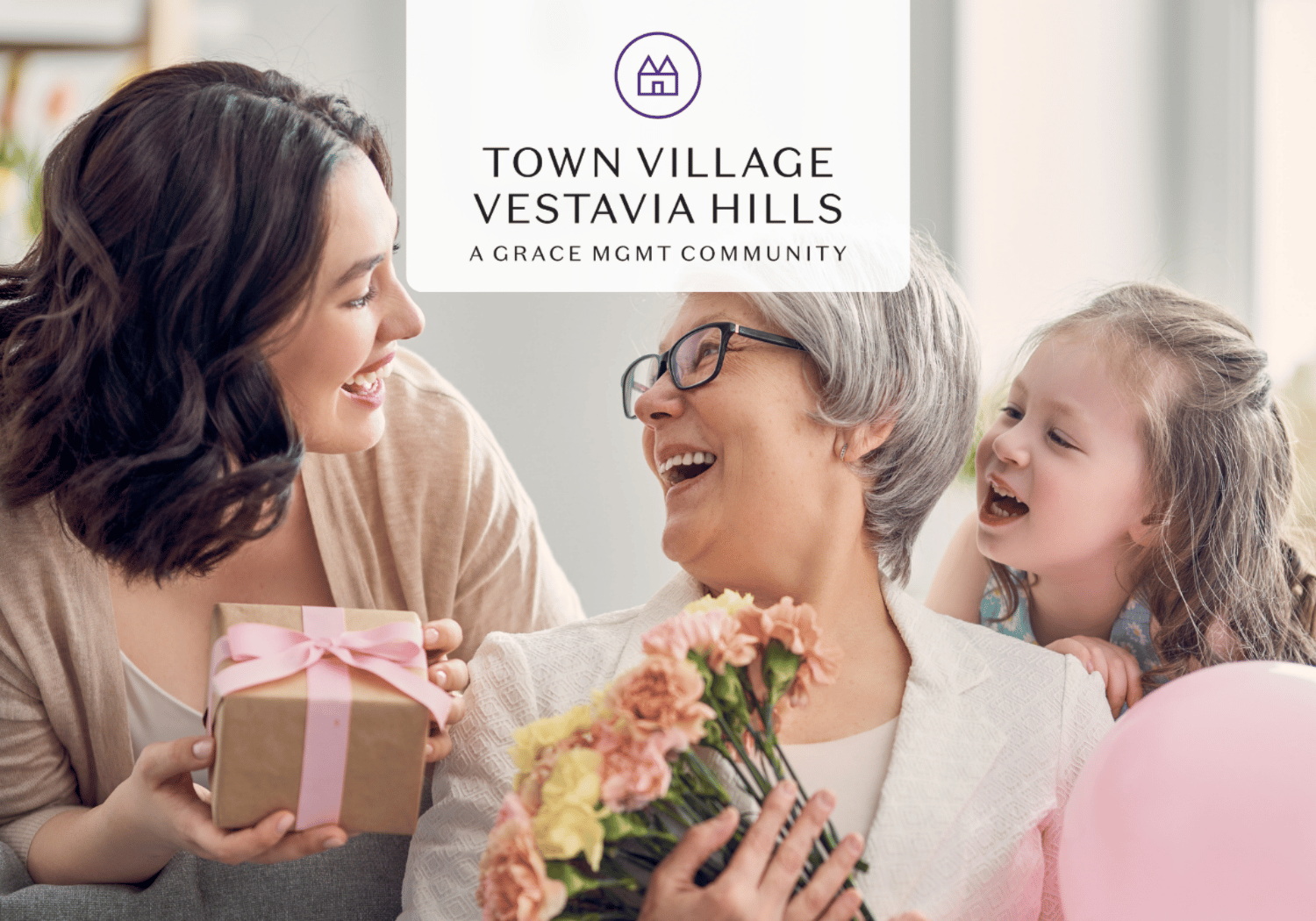 Three generations share a joyful moment: a younger woman hands a gift to an older woman holding flowers, while a child hugs nearby; logo overlay reads Town Village Vestavia Hills.