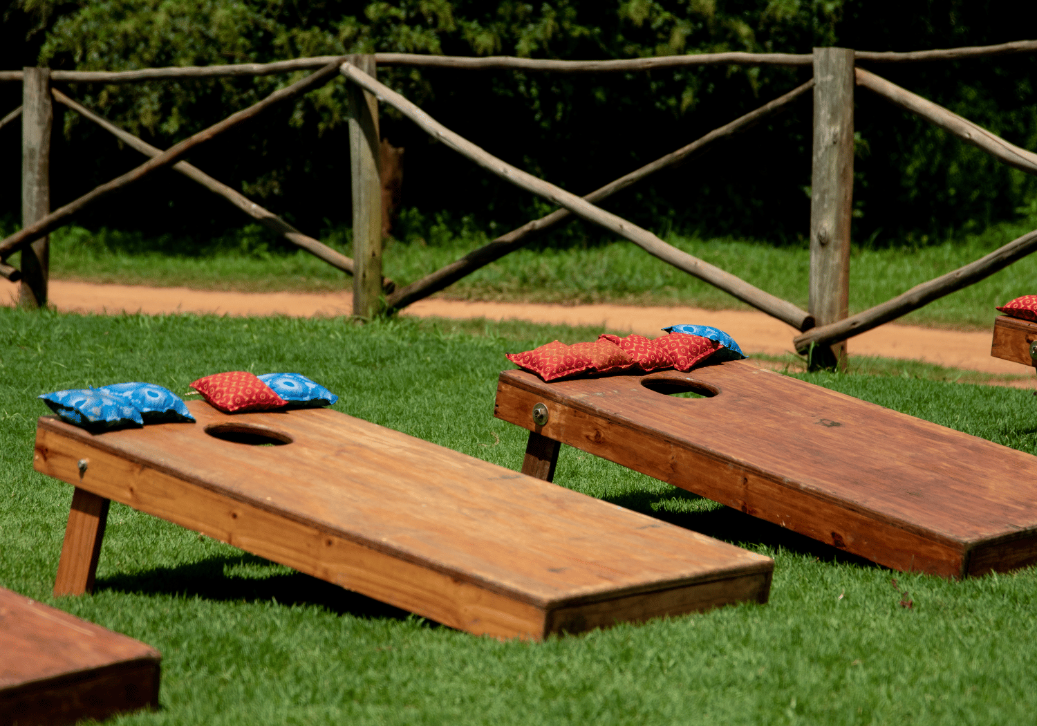 Outdoor lawn game setup with two wooden game boards and red and blue bean bags on top, holes in boards ready for tossing.