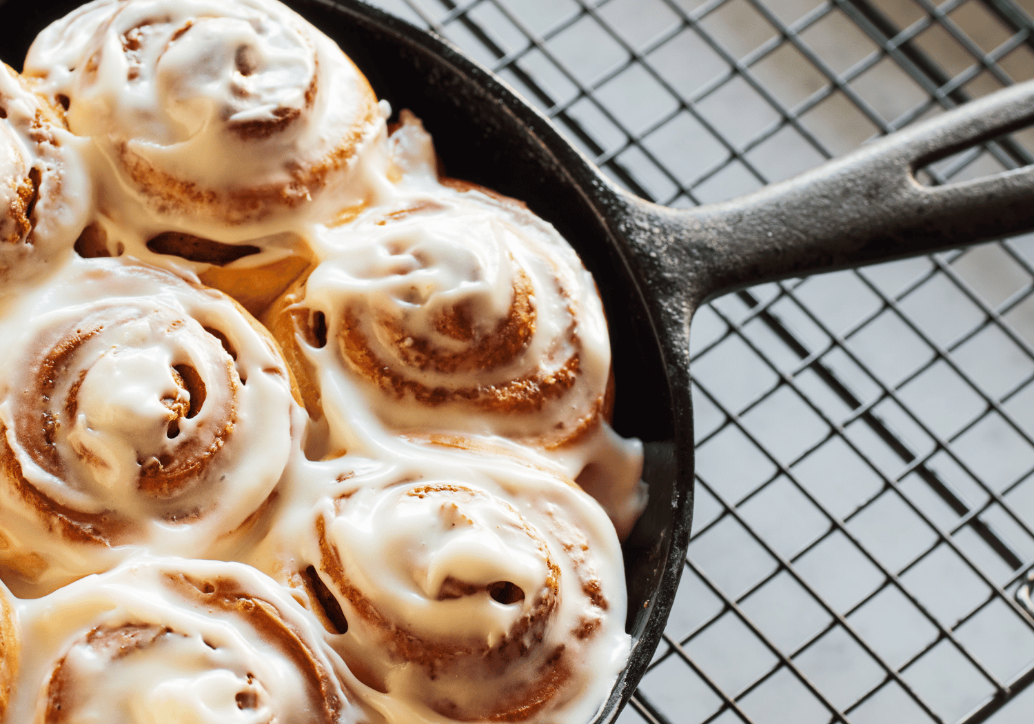 Cast-iron skillet filled with freshly baked cinnamon rolls, generously iced, resting on a wire cooling rack.